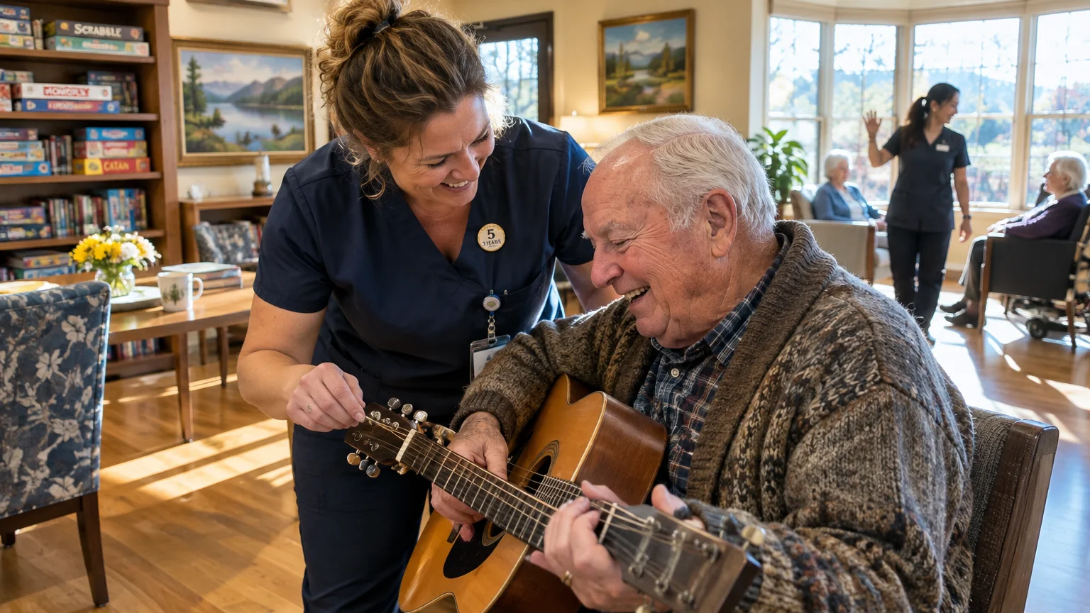 Smiling caregiver in scrubs assists an elderly resident holding an acoustic guitar in a senior living common room.